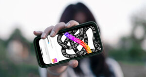 A girl blurred out in the background holding a phone in the foreground with the Instagram Threads logo on it.