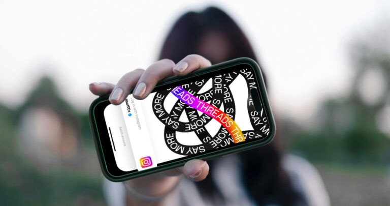 A girl blurred out in the background holding a phone in the foreground with the Instagram Threads logo on it.