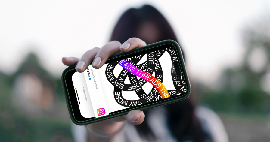 A girl blurred out in the background holding a phone in the foreground with the Instagram Threads logo on it.