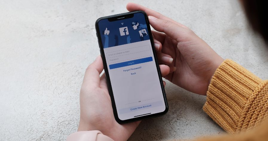 An arm with a yellow sweater holding a phone with the Facebook login screen