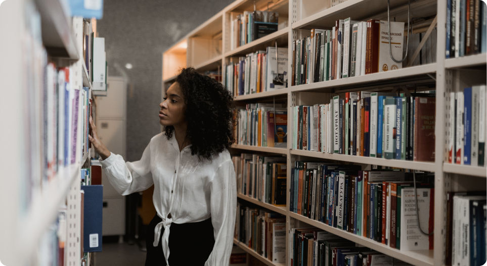 A girl in the aisle at the library looking at books on a shelf